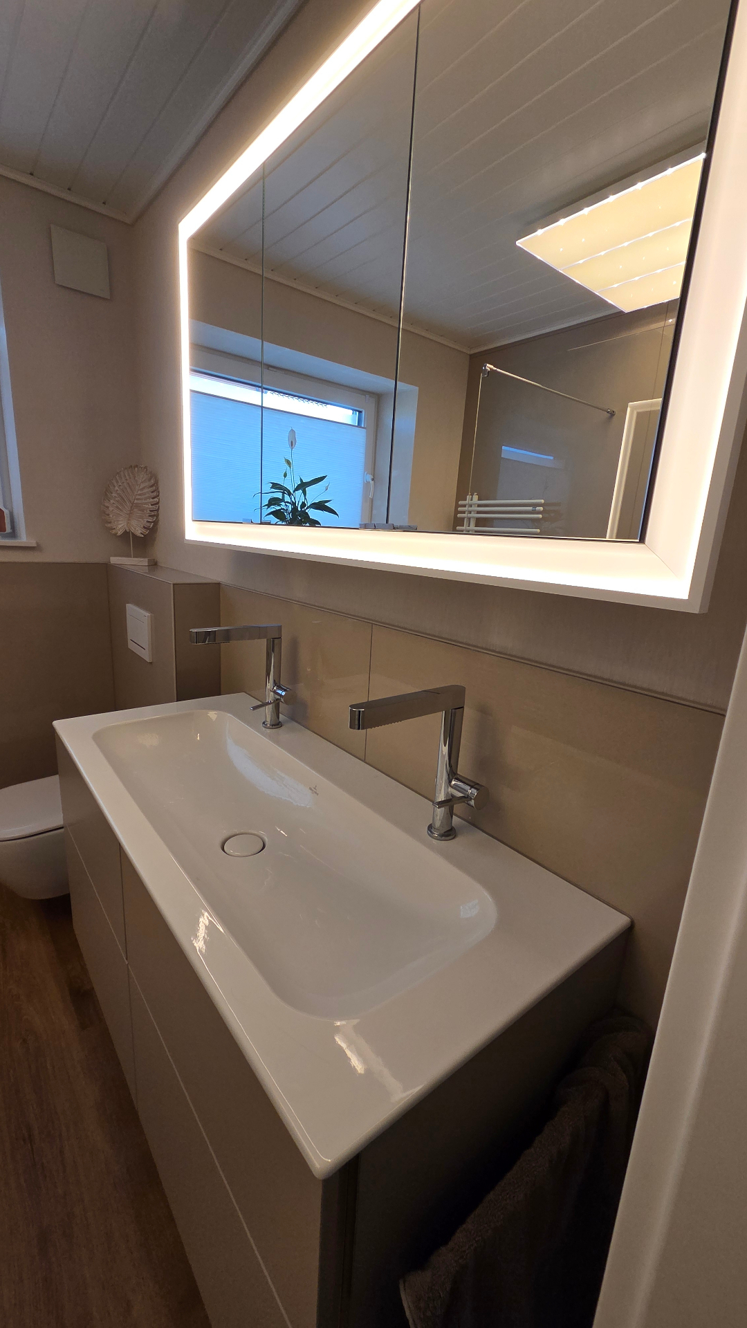 Modernes Badezimmer mit beleuchtetem LED-Spiegelschrank, weißem Doppelwaschbecken und beigefarbener Wandgestaltung