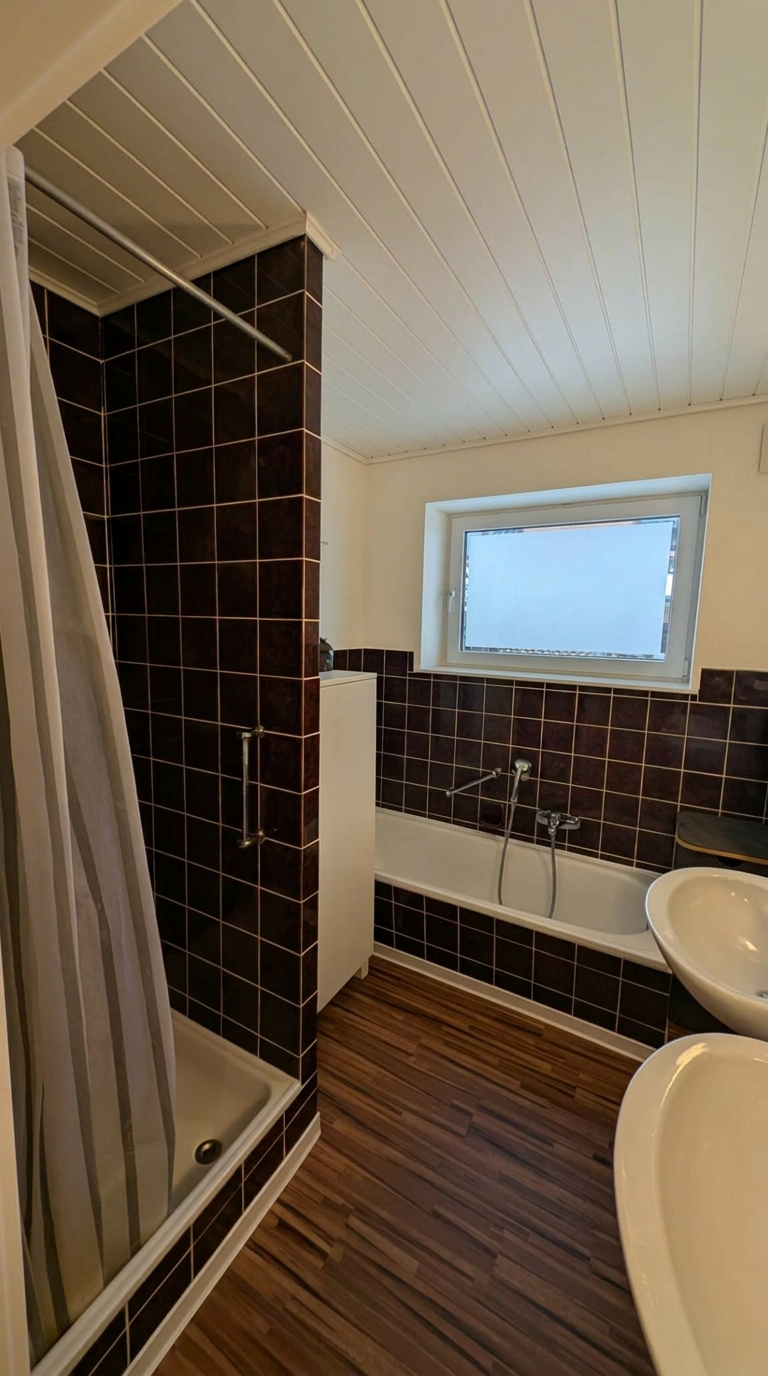 Altes Badezimmer mit dunklen Wandfliesen, Badewanne und Duschvorhang